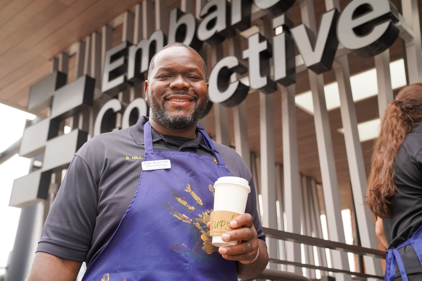 Tampa Police Captain Bryan Hill in a CUP apron holding a CUP cup outside the Downtown EMBARC location